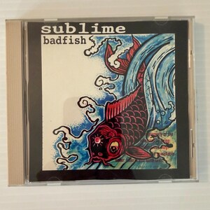 May include: CD case featuring the album "Badfish" by Sublime. The cover art displays a red and black koi fish with blue water elements. The band's name is in white text at the top.