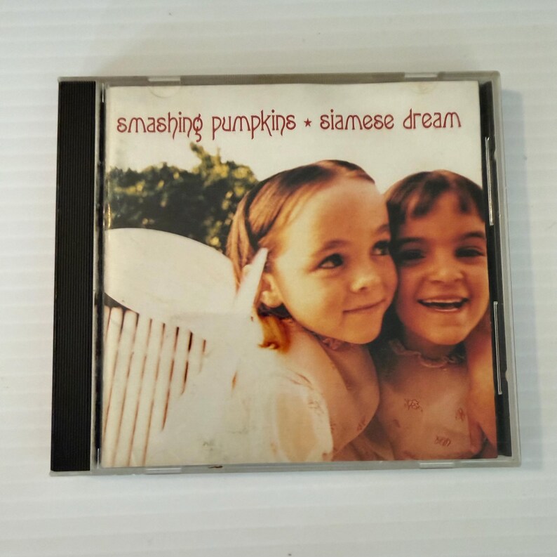May include: A CD case featuring the album "Siamese Dream" by The Smashing Pumpkins. The cover art displays two young girls. The album title and band name are in red text.
