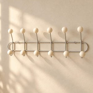 May include: A wall-mounted coat rack featuring a silver-toned metal frame with two horizontal bars. It includes six upward-facing hooks and six downward-facing hooks, each topped with a smooth, round, off-white ball at the end of every hook.