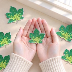 Op de afbeelding: Meerdere geborduurde esdoornblad-patches met een kleurverloop van donkergroen naar lichtgeelgroen. De patches hebben een gedetailleerde textuur met zichtbare stiklijnen die de natuurlijke nerven van een blad nabootsen, verspreid gerangschikt.