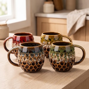 May include: Four ceramic mugs with rounded bodies and curved handles. Each mug features a reactive glaze with a honeycomb-like texture at the base, transitioning into a drip-effect pattern in red, yellow, brown, and green colour variations.