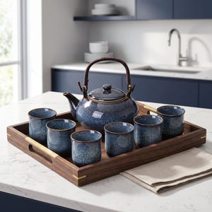 Pode incluir: Um conjunto de chá composto por um bule redondo de cerâmica azul salpicada com uma alça trançada castanho-escura e cinco chávenas de cerâmica azul salpicada a condizer. O conjunto está disposto num tabuleiro de servir retangular de madeira.