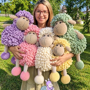 May include: Five plush sheep toys with textured, looped yarn bodies in purple, pink, cream, yellow, and green. Each sheep has a tan face, dark eyes, and matching colored feet. A logo at the bottom features a purple sheep and the text To Toys.