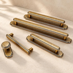 May include: A collection of antique brass cabinet hardware including three elongated rectangular drawer pulls with scalloped edges and a single round cabinet knob, all featuring a weathered metallic finish and grooved detailing.