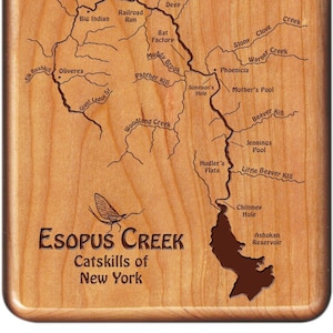 May include: A wooden plaque with a map of the Esopus Creek in the Catskills of New York. The map shows the creek's course, along with various tributaries and landmarks, including the Ashokan Reservoir, the Jennings Pool, and the Mother's Pool. The plaque also features a silhouette of a mayfly, a common insect found in the area.