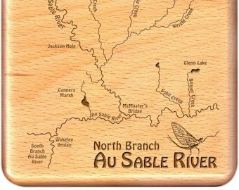 May include: A wooden map of the North Branch Au Sable River in Michigan, featuring the names of various lakes, creeks, and bridges. The map is surrounded by a brown wooden frame and includes a small image of a mayfly.
