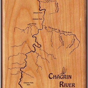 May include: A wooden plaque with a map of the Chagrin River in Ohio, featuring the names of various tributaries and points of interest, including Ward Brook, Gibson Park, Daniels Park, Gully Brook, Last Branch, Stoney Brook, Pierson Creek, and Chagrin Falls Dam. The plaque also features the text "Chagrin River" and a stylized image of a mayfly.