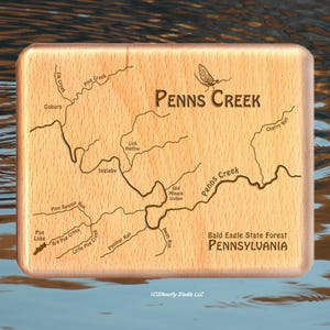 May include: A wooden sign with a map of Penns Creek in Bald Eagle State Forest, Pennsylvania. The map shows the creek winding through the forest, with various tributaries and features labeled. The sign also includes the text "PENNS CREEK" and "Bald Eagle State Forest PENNSYLVANIA".