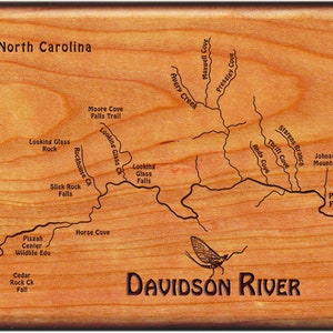 May include: A wooden plaque with a map of the Davidson River in North Carolina. The map shows the river's course, including various coves, creeks, and branches. The text "DAVIDSON RIVER" is engraved below the map, along with the words "North Carolina" and "Pisgah Forest".