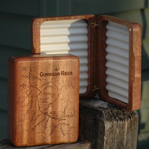 May include: A wooden fly fishing box with a map of the Gunnison River engraved on the lid. The box is open and shows the white foam interior.