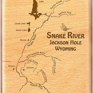 May include: A wooden map of the Snake River in Jackson Hole, Wyoming. The map shows the Snake River and its tributaries, as well as several lakes and creeks. The text "SNAKE RIVER JACKSON HOLE WYOMING" is engraved on the map.