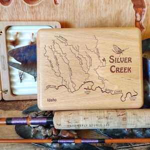 May include: A wooden box with an engraved map of the Silver Creek area in Idaho. The box is made of light wood and has a dark brown stain. The map shows the Silver Creek and its tributaries, including Grove Creek, Cane Creek, Mud Creek, Thompson Creek, and Stalker Creek. The box also has the words "Silver Creek" and "Idaho" engraved on it.