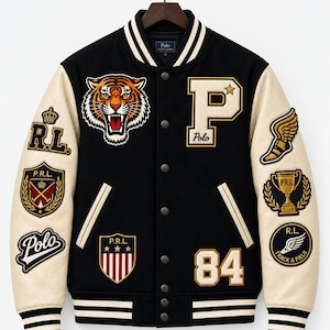 May include: A black varsity jacket with cream-colored sleeves, featuring a tiger head patch, a large letter P, and the number 84. The jacket includes various embroidered patches such as a shield, a trophy, and wings, with striped ribbed trim.