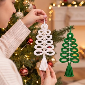 Könnte beinhalten: Zwei gehäkelte Weihnachtsbaumschmuckstücke, eines in Weiß und eines in Grün, bestehend aus gestapelten Schlaufen, einer zentralen vertikalen Reihe kleiner weißer Perlen und einer passenden Quaste am unteren Ende, aufgehängt an einer Schlaufe.