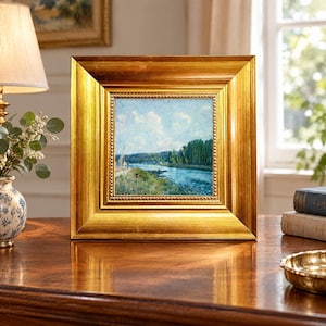 May include: A square landscape painting featuring a river, green trees, and a blue sky with white clouds, encased in a wide, ornate gold frame with a beaded inner border. The artwork depicts a serene outdoor scene with a small boat on the water.