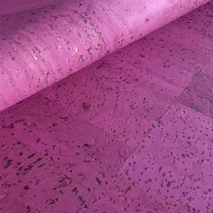 May include: A roll of vibrant magenta cork material. The cork has a textured surface with dark and light flecks throughout. The material is partially rolled, revealing the underside and the texture of the cork.