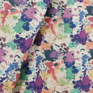 May include: A beige fabric with a colorful paint splatter pattern. The fabric has a textured surface that resembles cork.