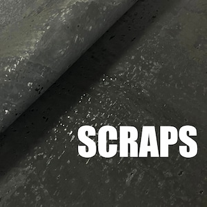 May include: A close-up of a dark grey textured fabric with the word "SCRAPS" printed in white.