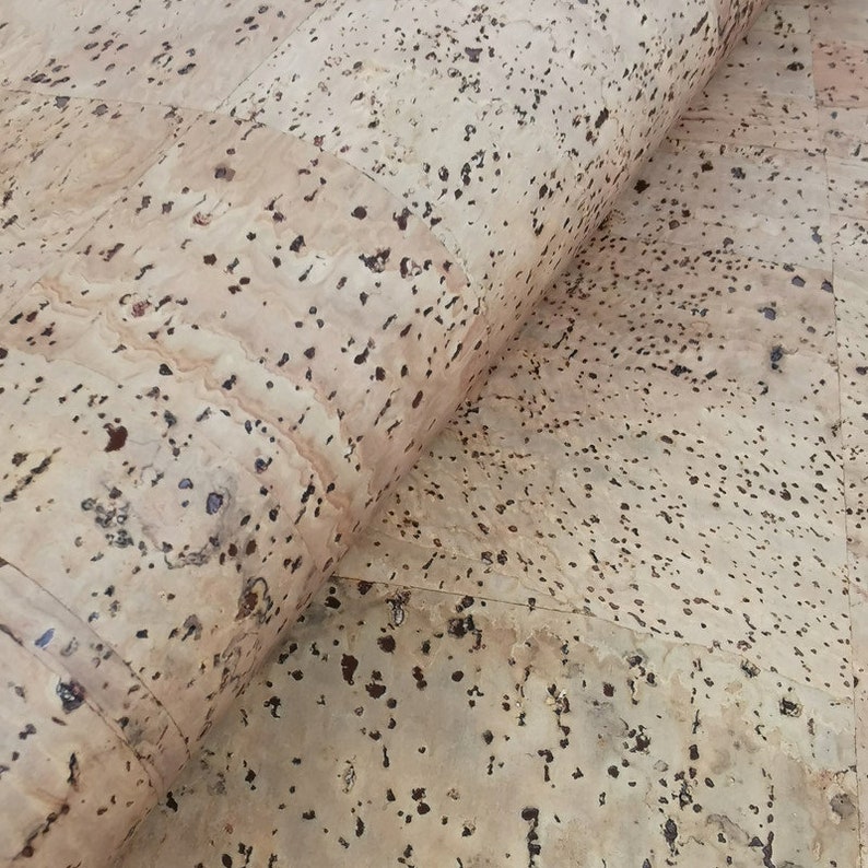 May include: A close-up of a roll of cork sheet with a natural beige colour and brown flecks. The cork is rolled up and the edges are visible.