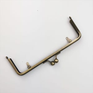 May include: A gold-toned metal purse frame with two clasps and two loops. The frame is designed to be used for a purse or clutch.