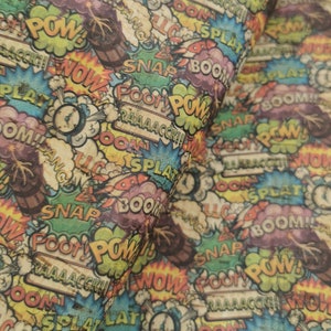 May include: A colorful fabric with a comic book pattern. The fabric features various words like "POW!" and "BOOM!" in different colors and styles.