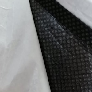 Peut inclure: Gros plan sur un mat&eacute;riau en couches. Une surface blanche et lisse est pli&eacute;e sur une couche noire textur&eacute;e. La couche noire pr&eacute;sente un motif de petits points en relief. L'image montre le contraste.
