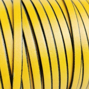 Puede incluir: Primer plano de un cordón de cuero amarillo con ribete negro. El cordón está enrollado y muestra la textura del cuero.