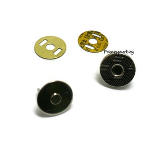 May include: A set of four silver magnetic snaps for sewing or crafting projects. The snaps have a round, flat design with a black patterned center. The set includes two male snaps and two female snaps.