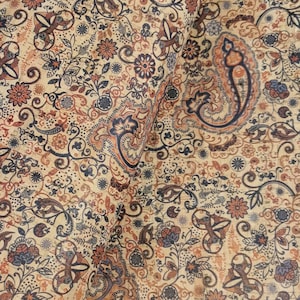 Può includere: Un tessuto beige con un motivo paisley in tonalità di blu, arancio e marrone. Il tessuto ha una superficie testurizzata che ricorda il sughero.
