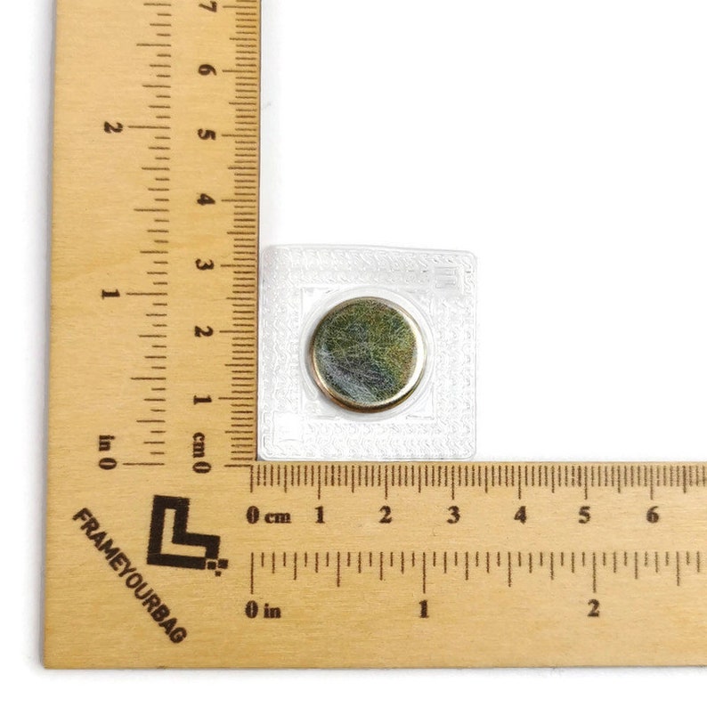 May include: A close-up of a small, round, silver magnet encased in a clear plastic square. The magnet is about 1 inch in diameter and is surrounded by a white border.