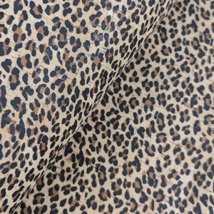 Puede incluir: Tela de corcho beige con un estampado de leopardo negro.