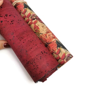 Puede incluir: Dos rollos de tela de corcho, uno con un patrón rojo moteado y el otro con una impresión floral con flores de hibisco rojas.