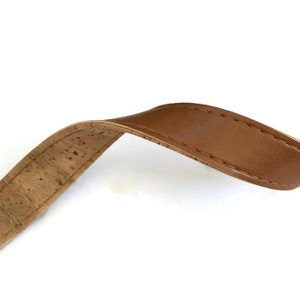 May include: A close-up of a brown cork and leather strap. The strap is made of a natural cork material on one side and brown leather on the other.
