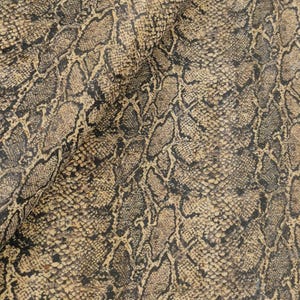 Könnte beinhalten: Nahaufnahme eines strukturierten Schlangenmuster in Braun-, Beige- und Schwarztönen. Das Material hat ein realistisches Reptilienschuppen-Design, wobei Farb- und Texturvariationen Tiefe und visuelles Interesse erzeugen. Der Stoff ist gefaltet.