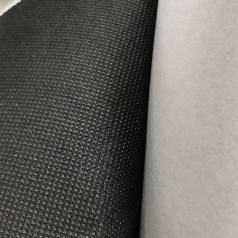 Peut inclure: Gros plan sur deux rouleaux de tissu. Un rouleau est noir avec un motif textur&eacute; en forme de losange. L'autre rouleau est blanc et lisse. Les tissus sont c&ocirc;te &agrave; c&ocirc;te, le tissu noir &agrave; gauche et le tissu blanc &agrave; droite.