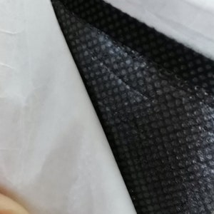 Peut inclure: Gros plan sur un tissu noir textur&eacute; avec un motif en forme de grille, partiellement recouvert d'un mat&eacute;riau blanc et lisse. Le contraste entre les deux mat&eacute;riaux cr&eacute;e une texture visuelle.