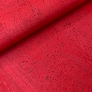 Könnte beinhalten: Roter Korkstoff mit gesprenkelter Textur. Der Stoff ist in der Mitte gefaltet und zeigt die Innenseite und Außenseite des Materials.