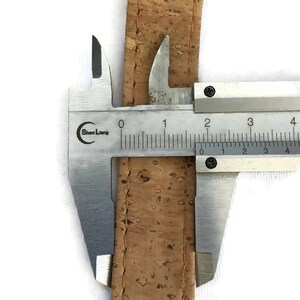 May include: A close-up of a cork strap measured with a caliper. The caliper reads 2 cm.