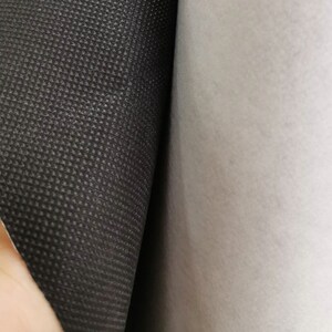 Peut inclure: Gros plan sur un rouleau de tissu noir textur&eacute; &agrave; c&ocirc;t&eacute; d'un rouleau de tissu blanc. Le tissu noir pr&eacute;sente un petit motif carr&eacute; r&eacute;p&eacute;titif. Le tissu blanc est lisse et semble &ecirc;tre un mat&eacute;riau semblable &agrave; du feutre.