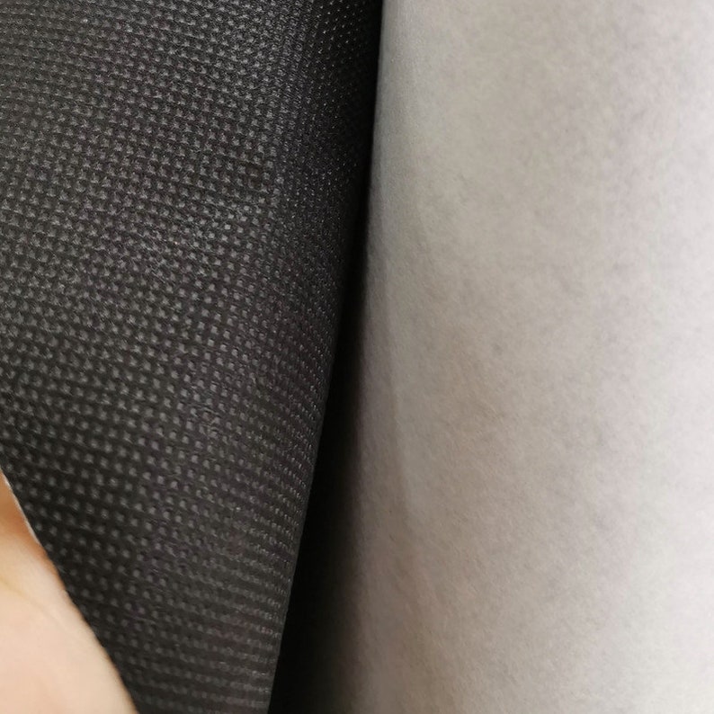 Peut inclure: Gros plan sur un rouleau de tissu noir textur&eacute; &agrave; c&ocirc;t&eacute; d'un rouleau de tissu blanc. Le tissu noir pr&eacute;sente un petit motif carr&eacute; r&eacute;p&eacute;titif. Le tissu blanc est lisse et semble &ecirc;tre un mat&eacute;riau semblable &agrave; du feutre.