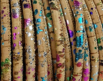 May include: Close-up of a roll of cork trim with a colorful, glittery pattern. The trim is beige with a silver, blue, pink, and green glitter pattern.