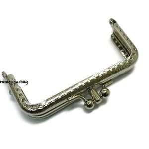 May include: Silver-toned metal purse frame with a decorative pattern and two small round clasps.