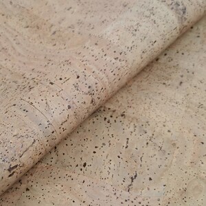 May include: Close-up of a sheet of natural cork with a light brown colour and a speckled texture. The cork is folded over, revealing the underside.
