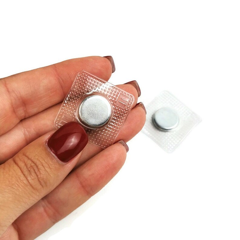 May include: Two clear plastic squares with a silver magnetic button inside each. The squares are designed to be sewn onto fabric.