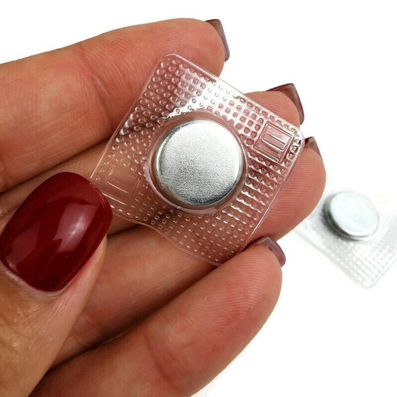 May include: Two clear plastic magnetic closures with silver metal discs. The closures are square shaped with a grid pattern.