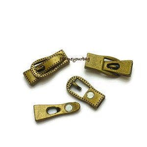 Könnte beinhalten: Vier antike goldfarbene Metallschließen mit einem gepunkteten Design. Die Schließen sind magnetisch und haben ein schnallenartiges Design.