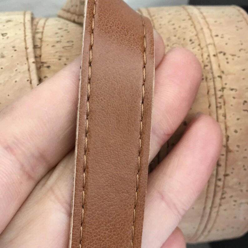 May include: Close-up of a brown leather strap with stitching along the edges. The strap is against a background of cork.