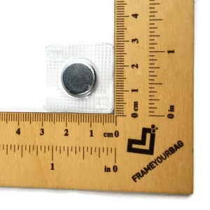 May include: A close-up of a clear plastic magnetic snap closure with a silver metal disc. The snap is measured against a ruler, showing it is approximately 1 cm in size.