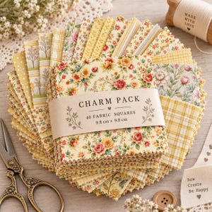 Op de afbeelding: Een charm pack van 40 stoffen vierkantjes van 9,8 cm bij 9,8 cm, met gele, crème en roze bloemen-, ruit- en stippenpatronen met gekartelde randen, verpakt in een papieren band met de tekst CHARM PACK 40 FABRIC SQUARES 9,8 cm x 9,8 cm.