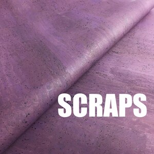 Puede incluir: Una hoja de tela de corcho morada con una textura natural moteada, doblada para mostrar la flexibilidad del material. La palabra SCRAPS está impresa en letras mayúsculas blancas, grandes y negritas en la parte inferior de la superficie morada.